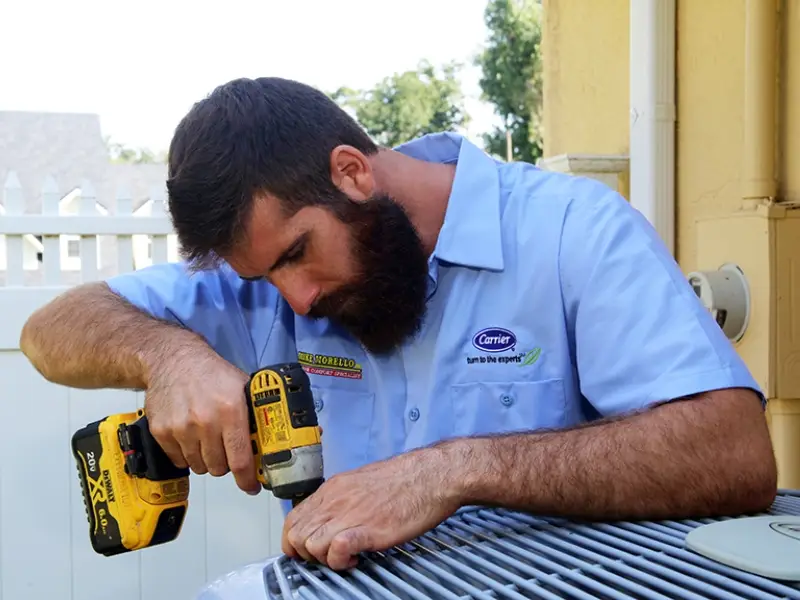 HVAC technician using a drill to perform HVAC repair services on an outdoor Carrier AC unit, ensuring proper cooling performance.