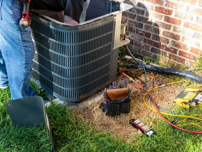 Technician performing HVAC repair services on an outdoor AC unit, using tools to diagnose and fix cooling system issues.